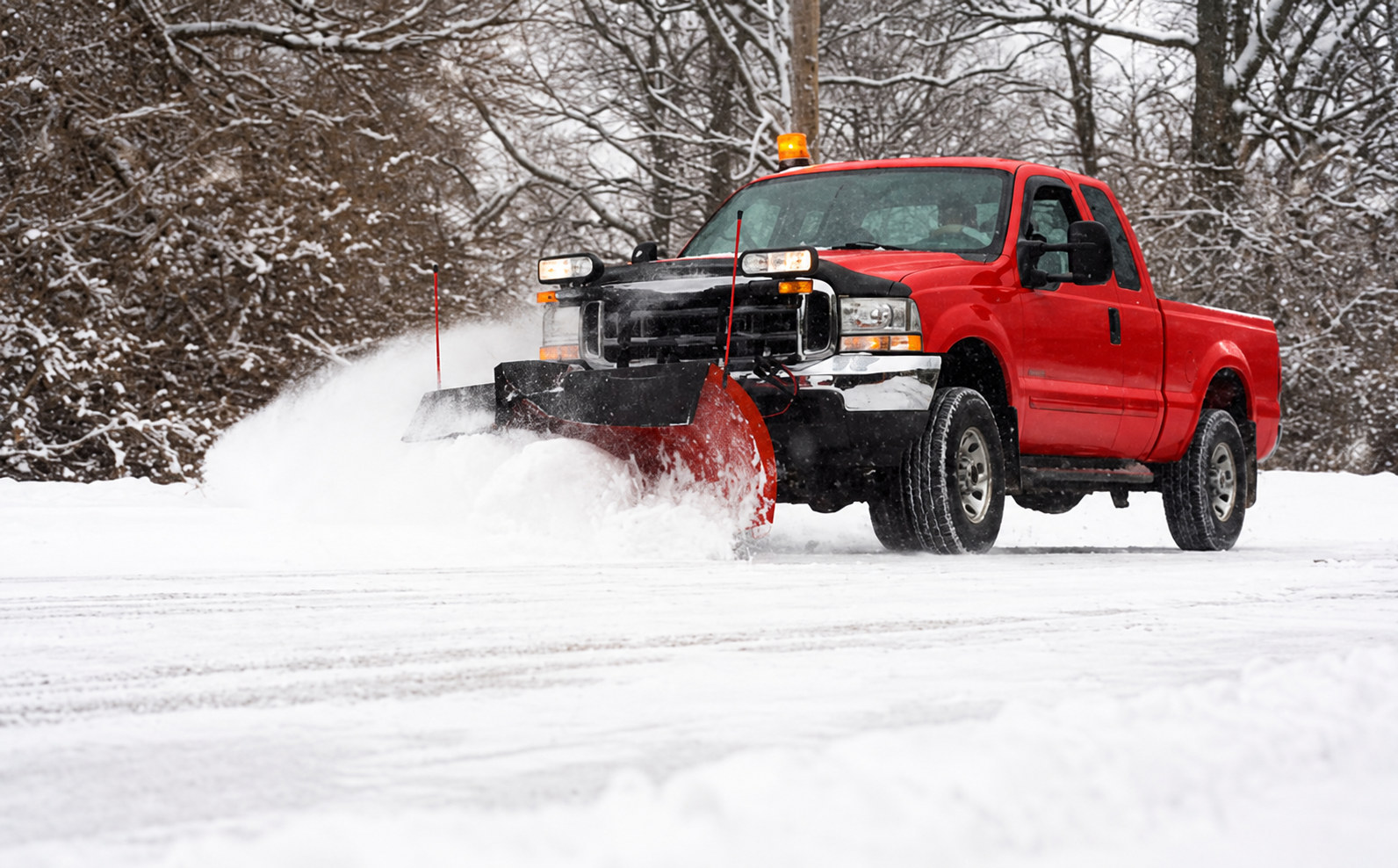 Red pickup truck clearing a snowy road with a front-mounted plow